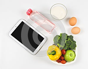 Blank black  screen computer tablet , vegetables and fruit in heart shape plate, bottle of water, a glass of milk, eggs on white