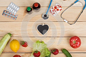 Blank blackboard in shape of heart, stethoscope and choice between natural vitamins, vegetables, fruits and berries or tablets and