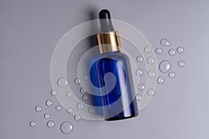 Blank blue glass essential oil bottle with pipette on gray background decorated waterdrops. Skin care concept with