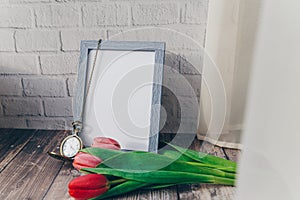 blank blue photo frame with vintage round clock and tulips on brick wall background