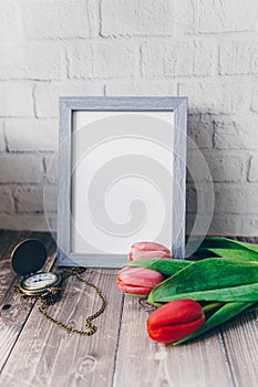 blank blue photo frame with vintage round clock and tulips on brick wall background