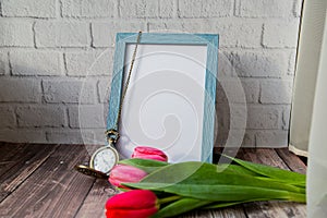 blank blue photo frame with vintage round clock and tulips on brick wall background