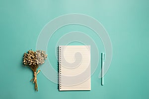 A blank book with flower and pen on a green background with copy space.