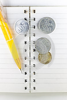 Blank book and yellow pen with coins on an  white background.