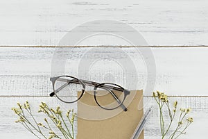 Blank brown card, pen and eyeglasses decorated with yellow limonium caspia flowers