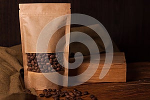 Blank brown kraft paper pouch bag with coffee beans in transparent window on wooden background. Trendy packaging for tea