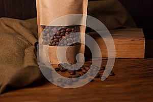 Blank brown kraft paper pouch bag with coffee beans in transparent window on wooden background. Trendy packaging for tea
