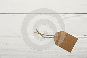 Blank brown price tag on on white wooden background. View from above. Blank brown cardboard price tag or label  on white b