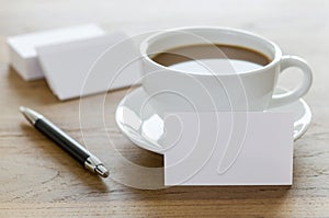 Blank business cards, pen and cup of coffee on wooden table.