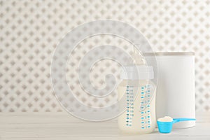 Blank can of powdered infant formula with feeding bottle and scoop on white wooden table, space for text. Baby milk