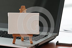 Blank canvas and wooden easel on laptop computer