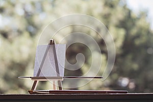 Blank canvas on wooden mini easel in front of nature and paint brushes, art work and inspiration concept