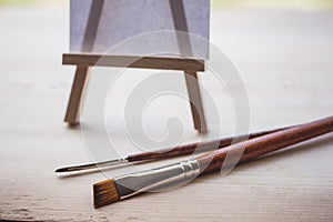Blank canvas on wooden mini easel in front of nature and paint brushes, art work and inspiration concept
