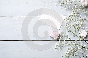 Blank card for invitation or congratulation, little gift box, bunch of gypsophila flowers on light blue wooden table. Banner mocku