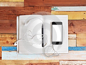 Blank cell phone, notebook and headphones on a wooden background