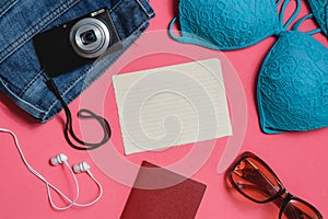 Blank Check list, Passport, Swimsuit, Jeans, Sunglasses, Photo Camera on Pink Background. Top View Travel Concept.