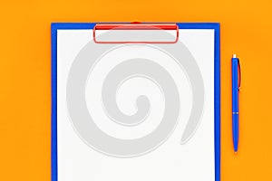 Blank clipboard mockup and blue pen on orange color background. Top view, copy space. Back to school, deadline, morning concept