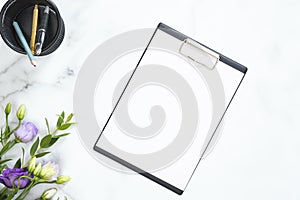 Blank clipboard mockup, stationery, flowers bouquet on marble background. Flat lay, top view minimalistic home office desk.