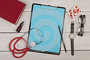 blank clipboard, pills, book, stethoscope, eyeglasses and watch on wooden background