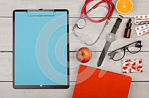 blank clipboard, pills, fruits, book, stethoscope, eyeglasses and watch on wooden background