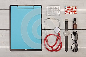 blank clipboard, pills, stethoscope, eyeglasses and watch on wooden background