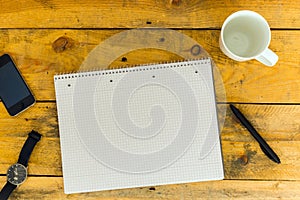 Blank College Writing Block, Pen, empty Coffee Mug, wristwatch and mobile phone on rustic wooden table, top view