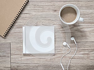 Blank compact disc , arphones,notebook and coffee on wooden background