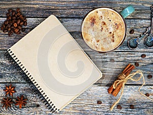 Blank craft sketchbook with cup of coffee, spoon and anise, cinnamon, beabs of coffe on vintage wooden table. Flat lay photo