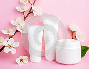 Blank cream bottles with spring flowers on pink background. Organic skincare concept with copy space. Cosmetics spa mockup