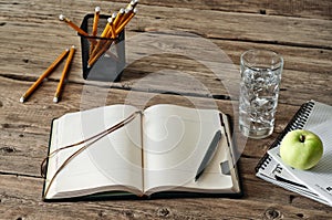 Blank diary on wooden table with a glass of water, apple and pencil closeup