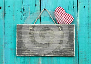 Blank distressed wood sign with red checkered heart hanging on rustic antique teal blue door