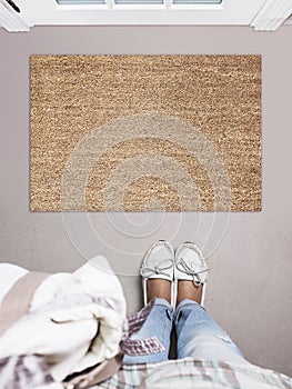 Blank doormat before the door in the hall. Mat on gray floor, girl in white shoes. Welcome home, product Mockup photo