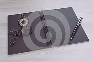 Blank empty black page note book opening with pen and vintage pocket watch on gray wooden table using as time, journal thinking,