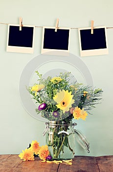 Blank empty instant photos hang on a rope over summer bouquet of flowers on the wooden table with mint background. vintage