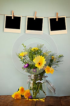 Blank empty instant photos hang on a rope over summer bouquet of flowers on the wooden table with mint background. vintage