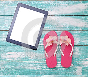 Blank empty tablet computer on beach. Trendy summer accessories on wooden background pool. Flip-flops on beach. Tropical flower or