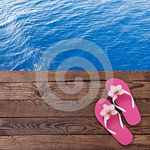 Blank empty tablet computer on beach. Trendy summer accessories on wooden background pool. Flip-flops on beach. Tropical flower or