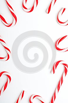Blank frame with Christmas candy canes top view. New Year lollipops on white background. Winter holidays backdrop with copyspace.