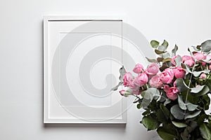 Blank frame mockup with passe-partout hanging on white wall and pink flowers in interior. White frame and floral decor