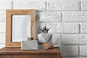 Blank frame and succulent plants on wooden  near white brick wall, space for design. Home decor