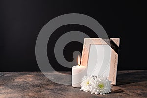 Blank funeral frame, candle and flowers on table against black background