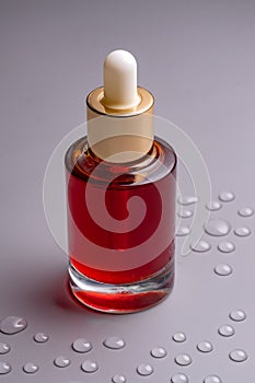 Blank glass essential oil bottle with pipette on gray background decorated water drops. Skin care concept with natural