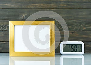 Blank golden frame and digital alarm clock on table