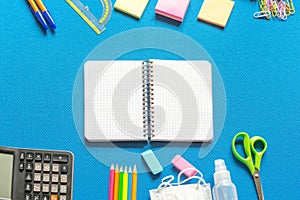 Blank graphing paper notebook with school supplies frame against a bright blue wall. Copy space.banner.advertisement