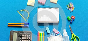 Blank graphing paper notebook with school supplies frame against a bright blue wall. Copy space.banner.advertisement