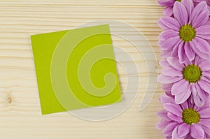 Blank green card and pink flowers on wooden background
