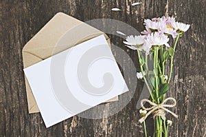 Blank greeting card with brown envelope and Mum flowers on wooden table