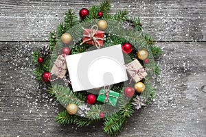 Blank greeting card in christmas wreath with decorations and gift boxes on rustic wooden table covered with snow