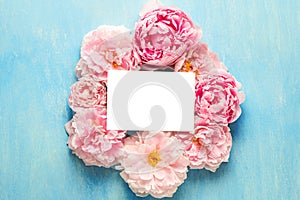 Blank greeting card in frame made of pink peony flowers on blue background. Flower composition. Mock up. Top view