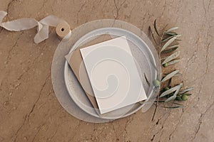 Blank greeting card, invitation and envelope mockup on ceramic plate. Beige marble stone tiles background with olive